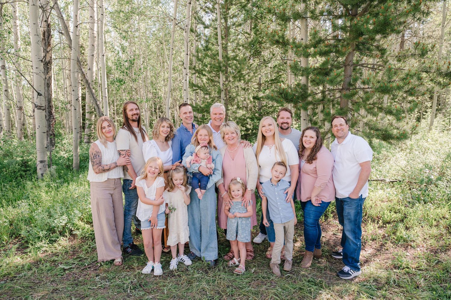 A group wearing coordinated casual outfits poses together in a sunlit forest setting during a summer photo session.