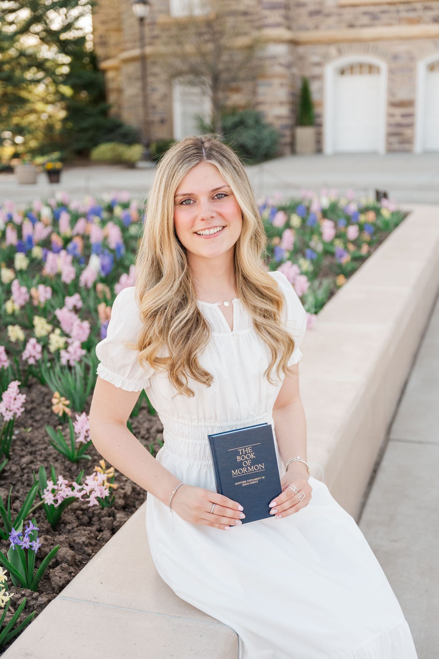Person in white dress with book near spring tulip garden.