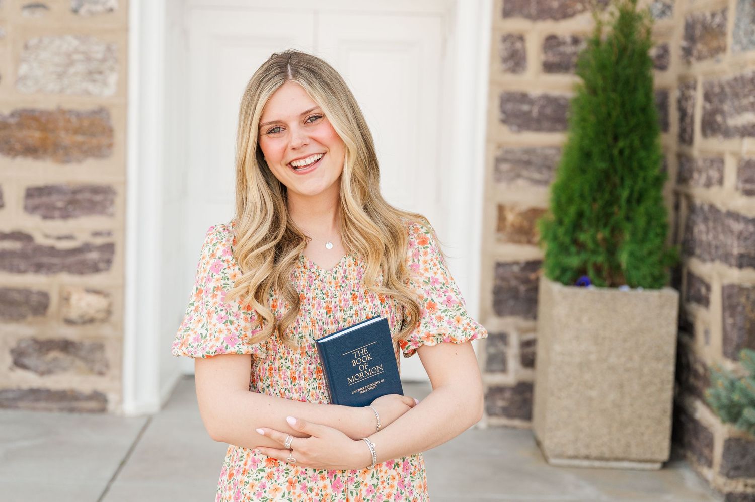 Someone in floral dress holding a blue book outside stone building.