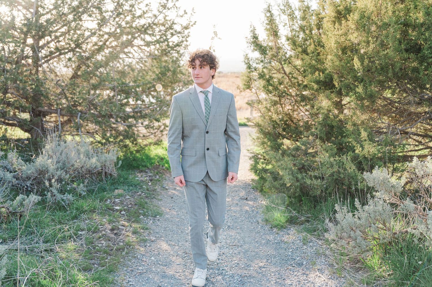 Person in gray suit walking along a nature path surrounded by greenery.