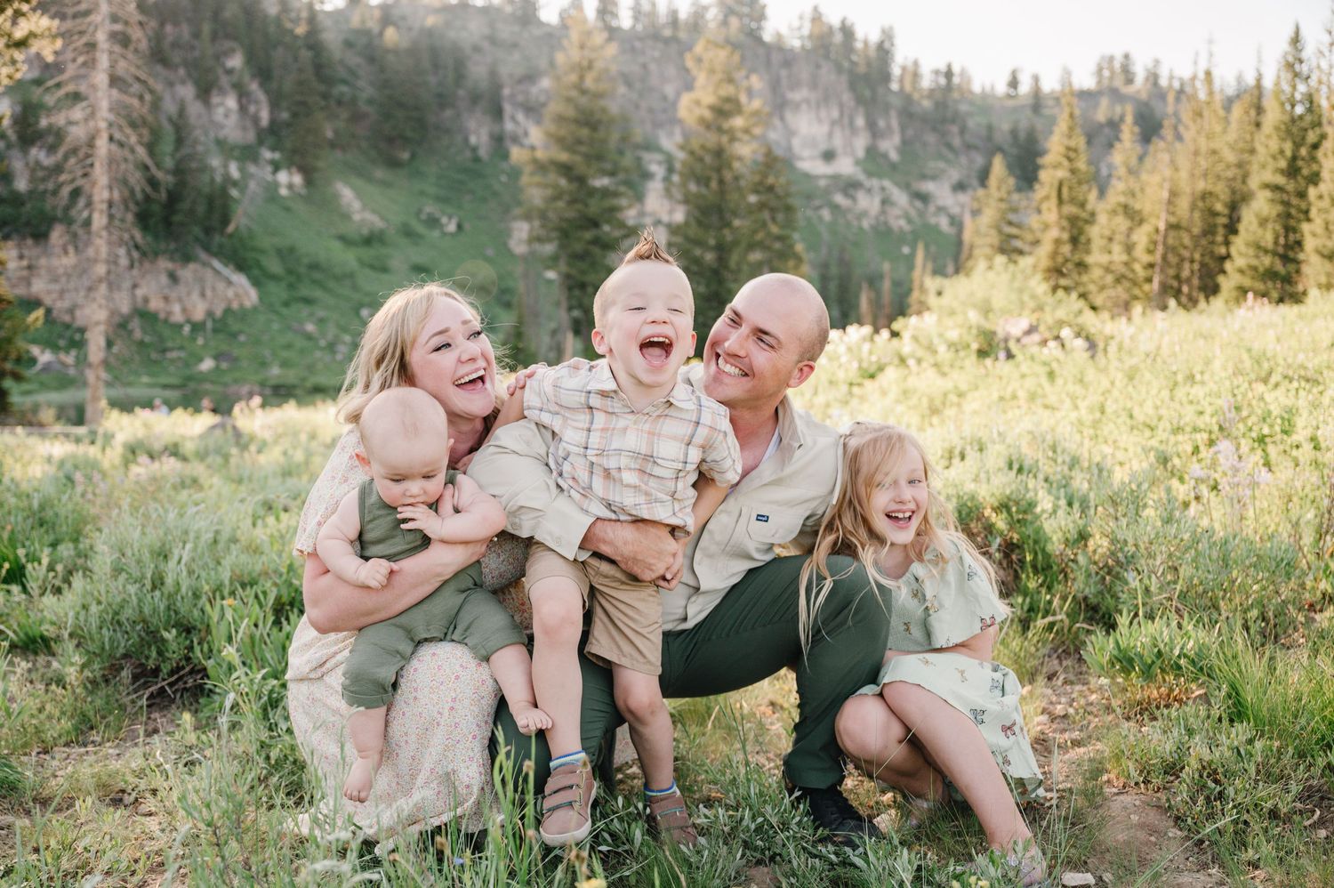 A joyful outdoor family portrait taken in a lush mountain setting during golden hour.