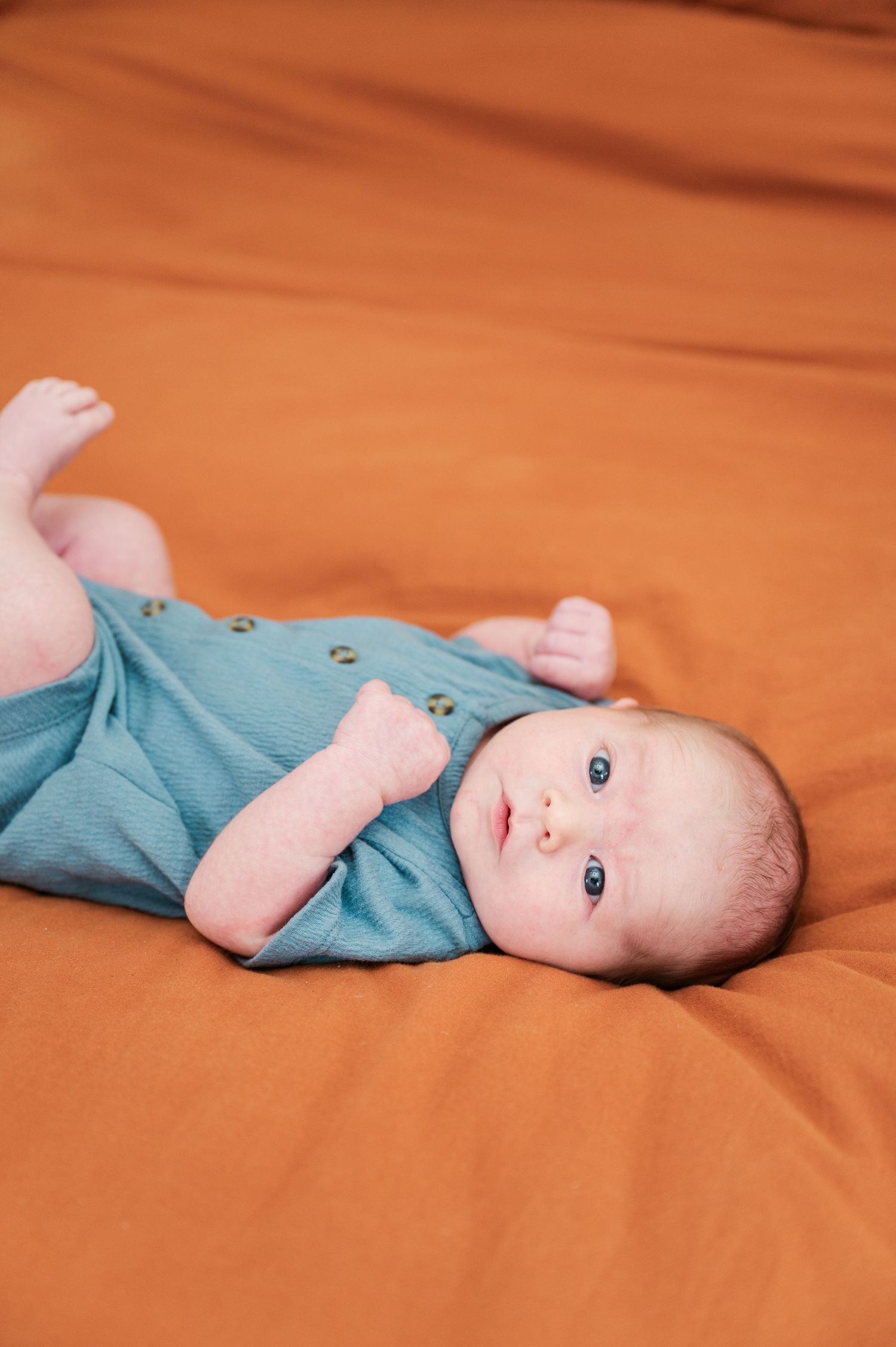 Baby wearing light blue onesie lays on orange bedding.
