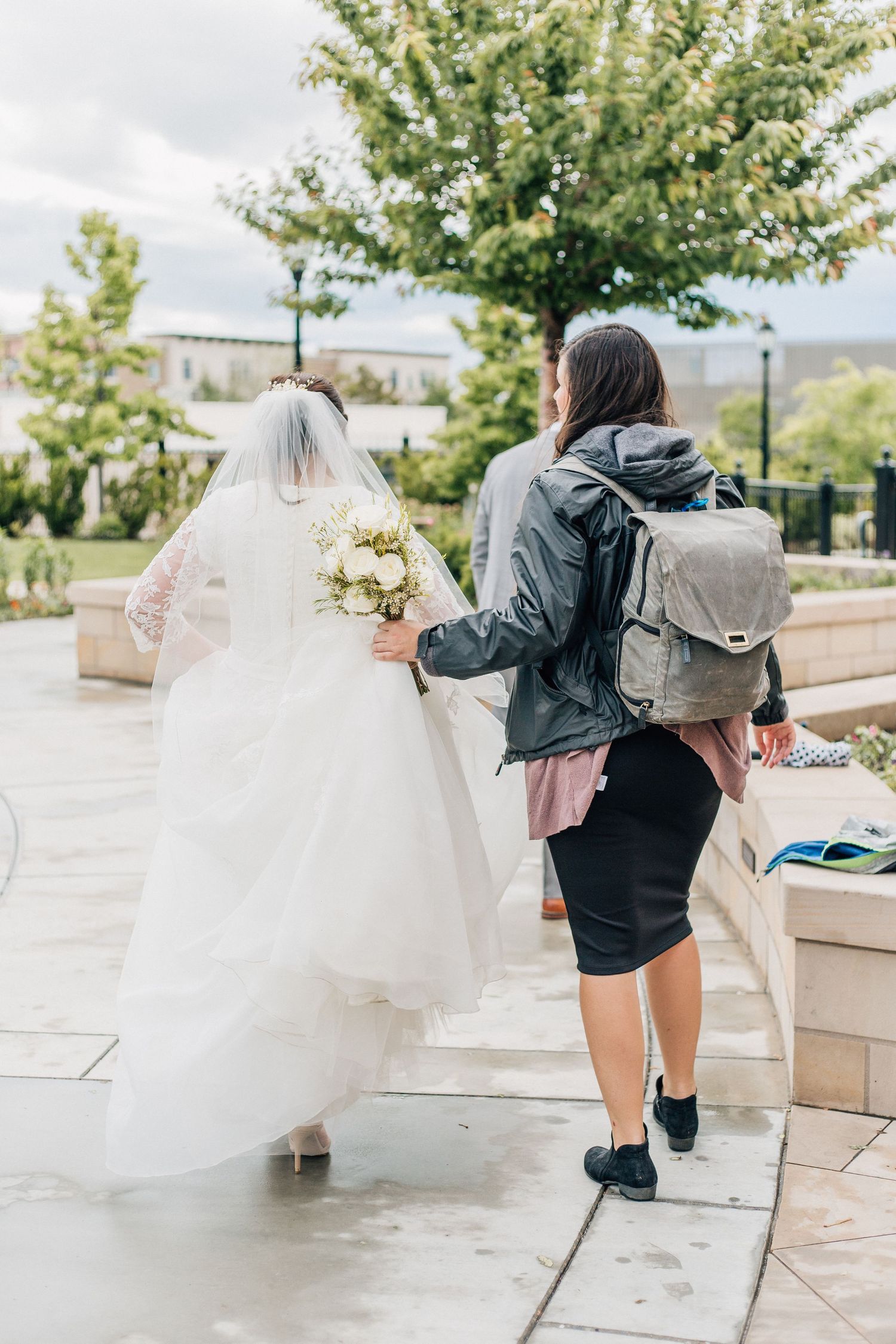 A wedding photographer follows behind a bride in a flowing white dress carrying a bouquet.