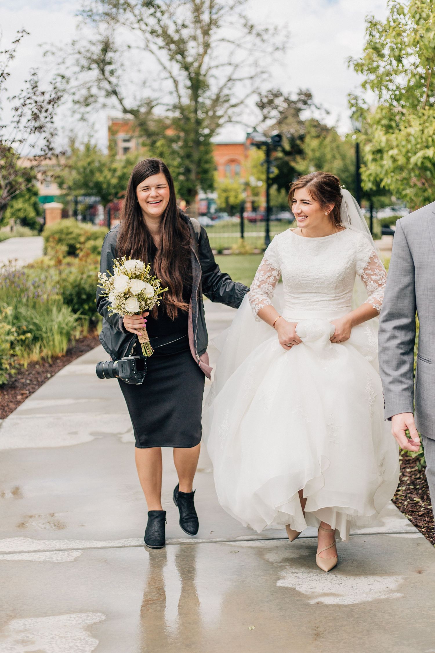 Wedding party walking and laughing together on a wet sidewalk surrounded by garden landscaping.