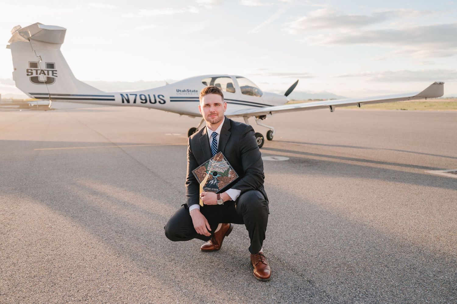 Person in business attire kneeling on tarmac next to a small private aircraft at sunset.