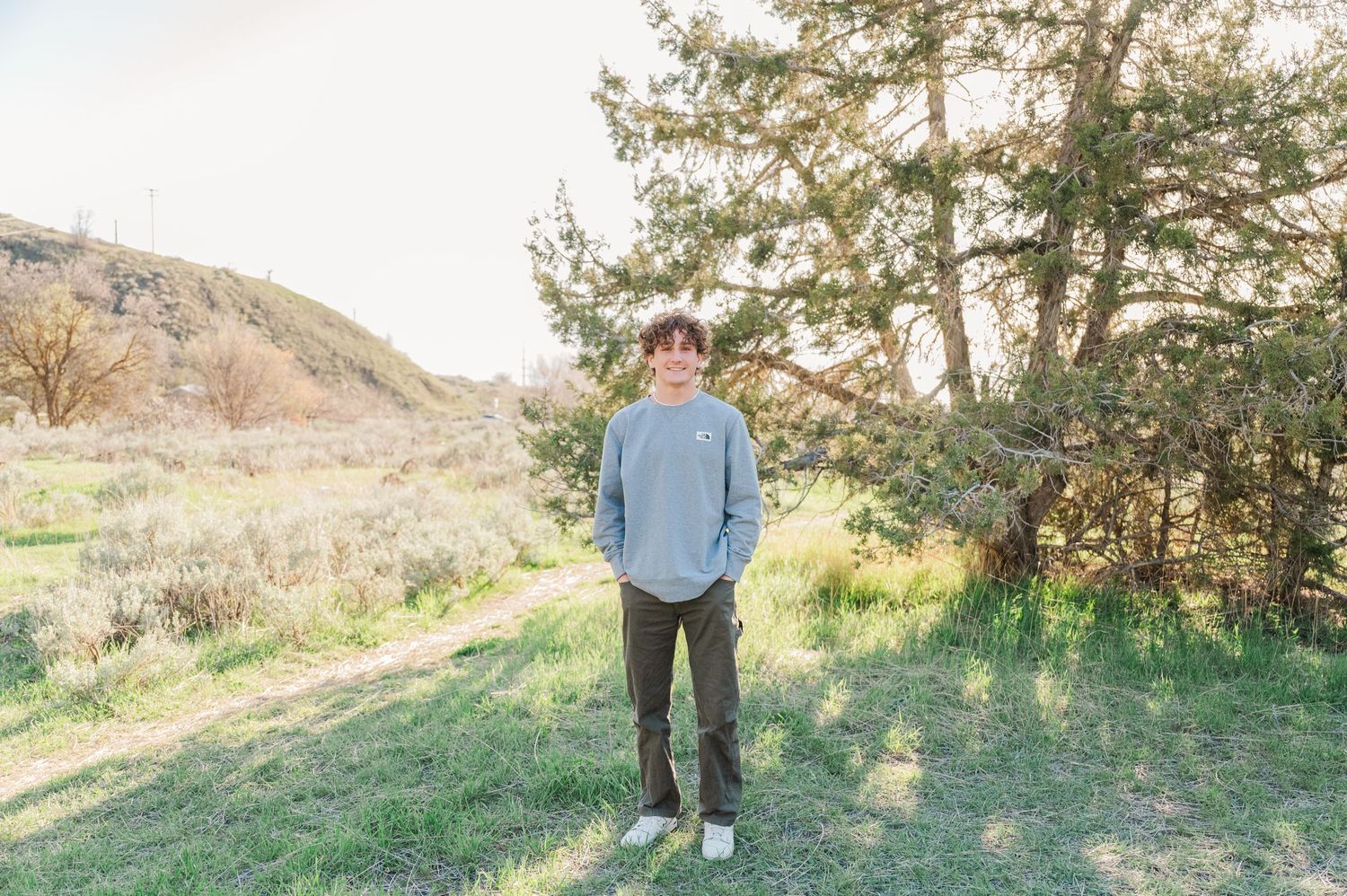 Casual figure in blue sweater standing on grassy hillside with scenic mountain view.