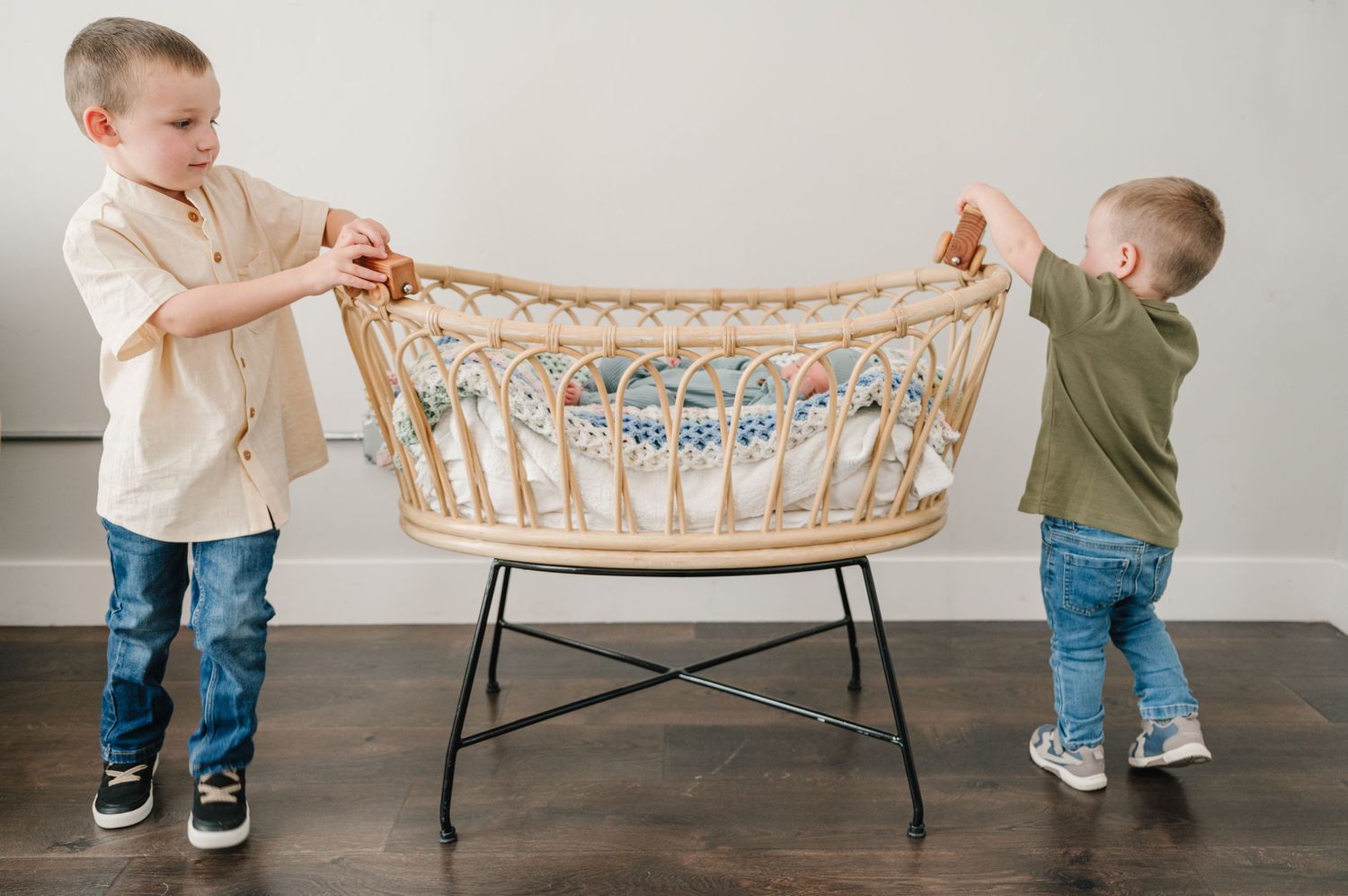 Two young children examining a wooden bassinet in an indoor setting.