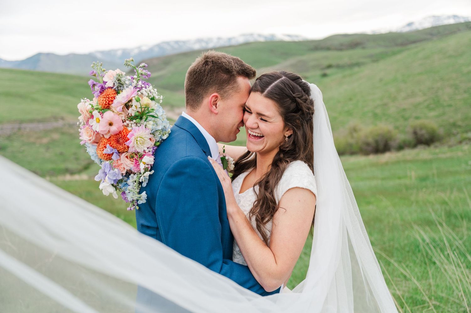 Romantic wedding couple embraces in mountain meadow with colorful wildflower bouquet.