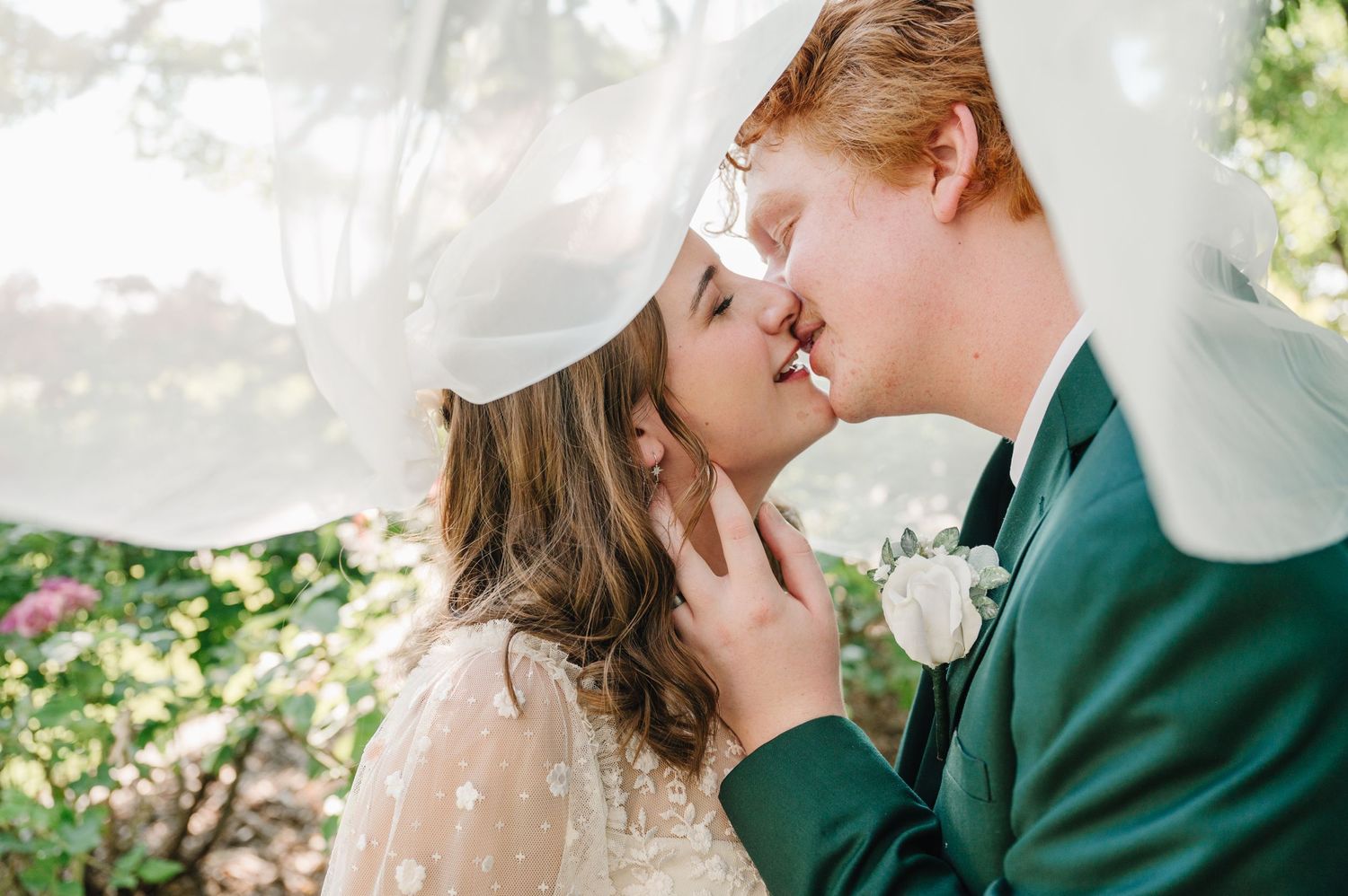 A romantic moment under flowing white fabric with greenery in the background.