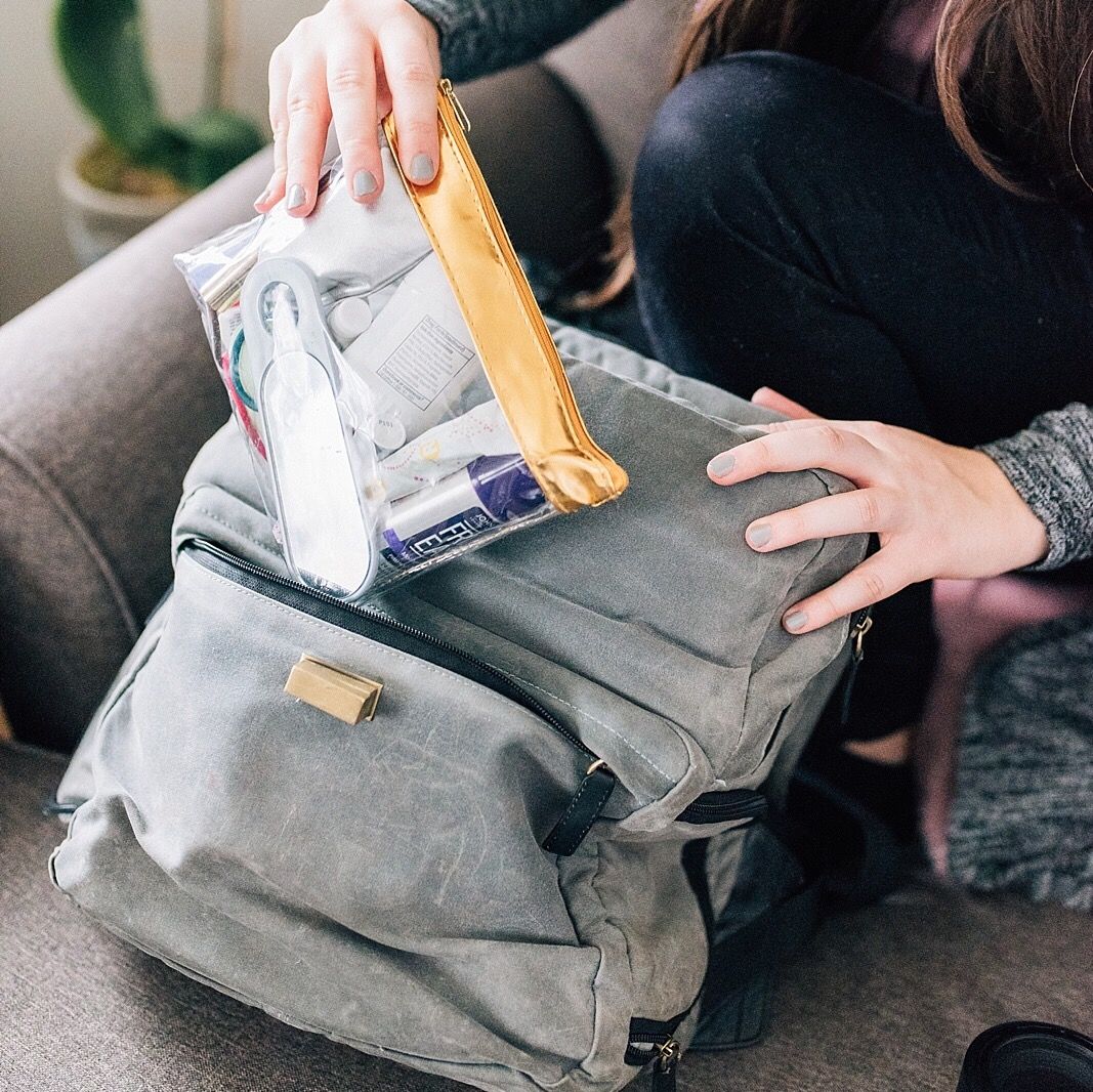 A grey backpack being packed with essentials using a packing cube organizer.