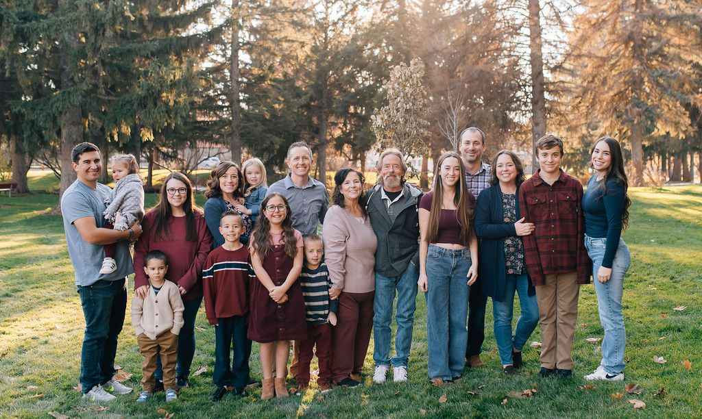 A group of people standing together outdoors in casual attire for a group photo in front of trees during golden hour.