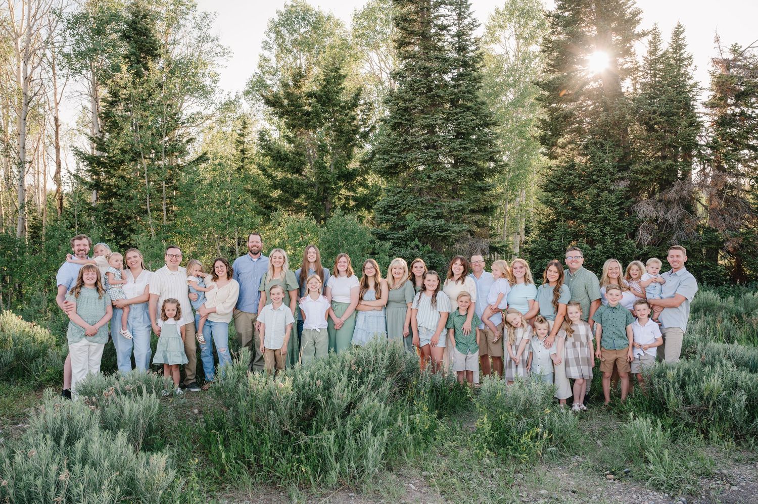 Large extended family group photo with everyone wearing coordinated white and blue outfits in a mountain meadow.