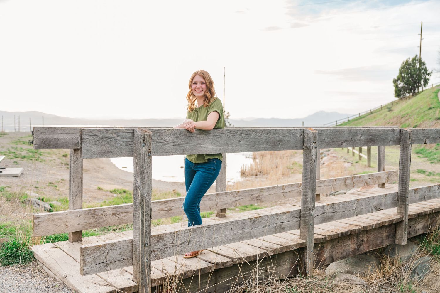 Person leaning on wooden fence railing in rural desert landscape.