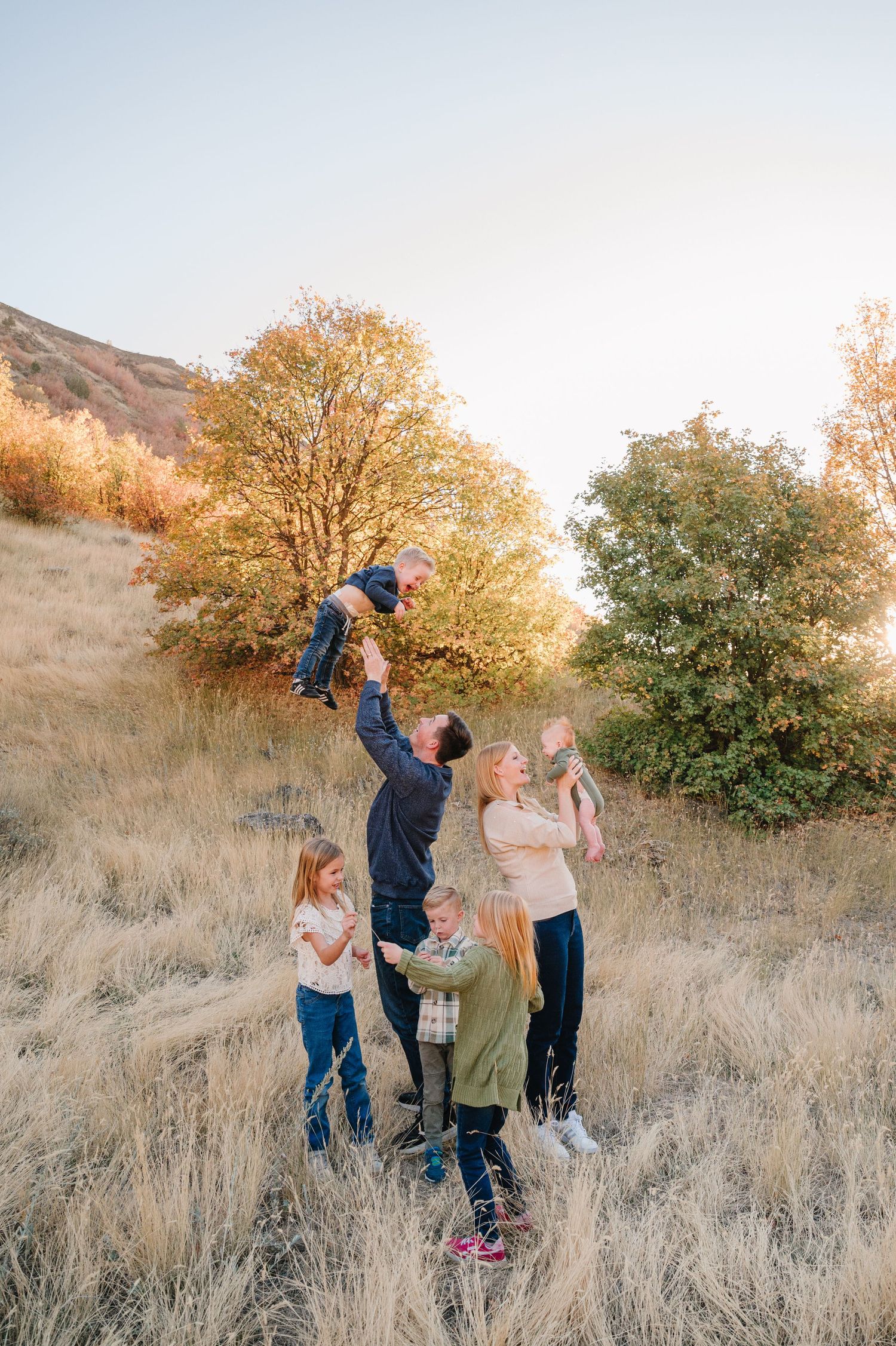 A family shares joyful moments together in a golden autumn field during sunset with tall dry grass and trees.