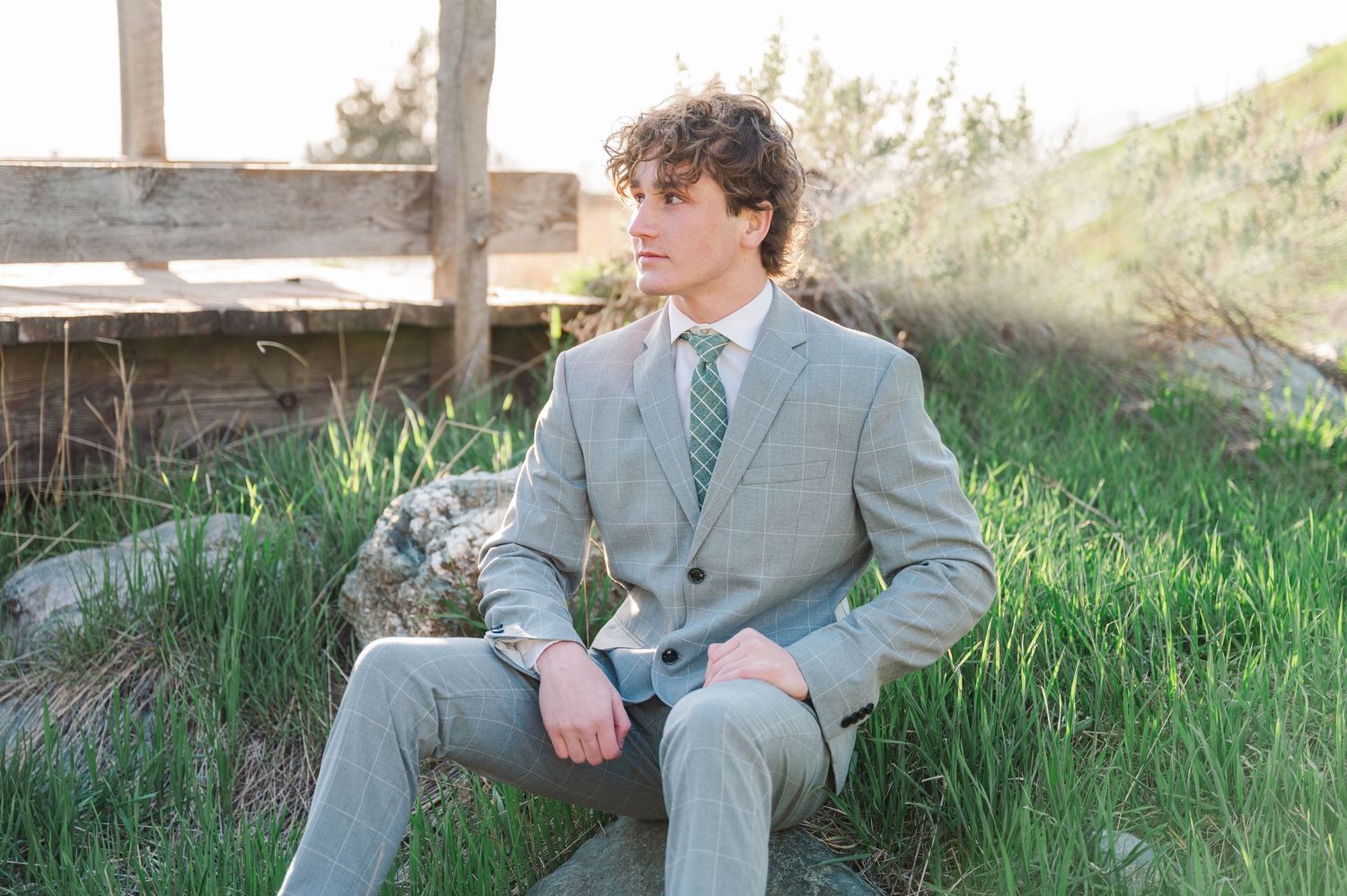 Outdoor portrait of someone in a light gray suit sitting in green grass.