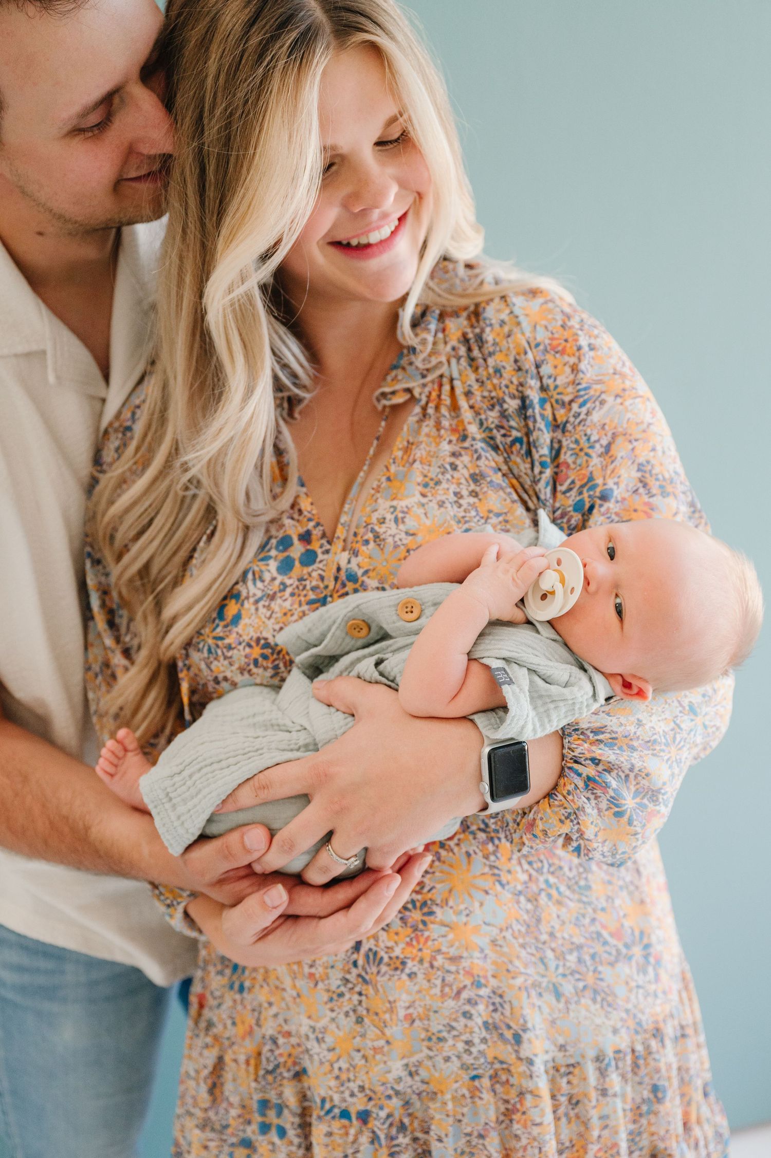 A tender moment as parents cradle their newborn baby against a light blue background.