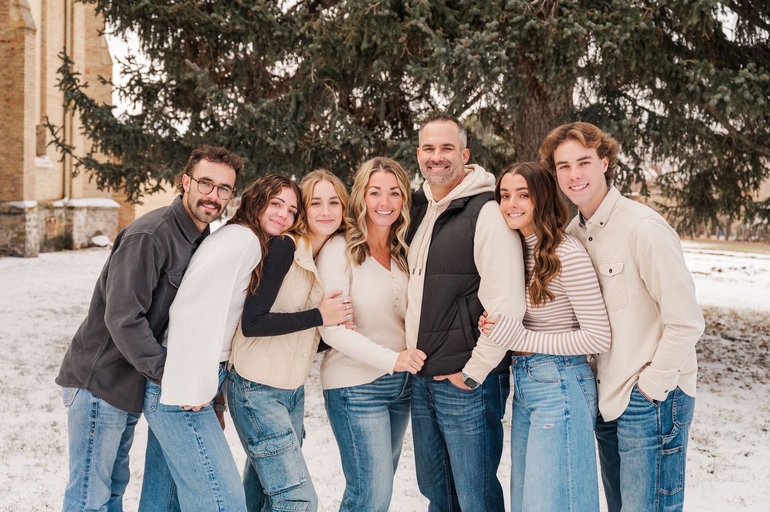 A group in coordinated winter outfits with jeans and sweaters poses together in the snow.