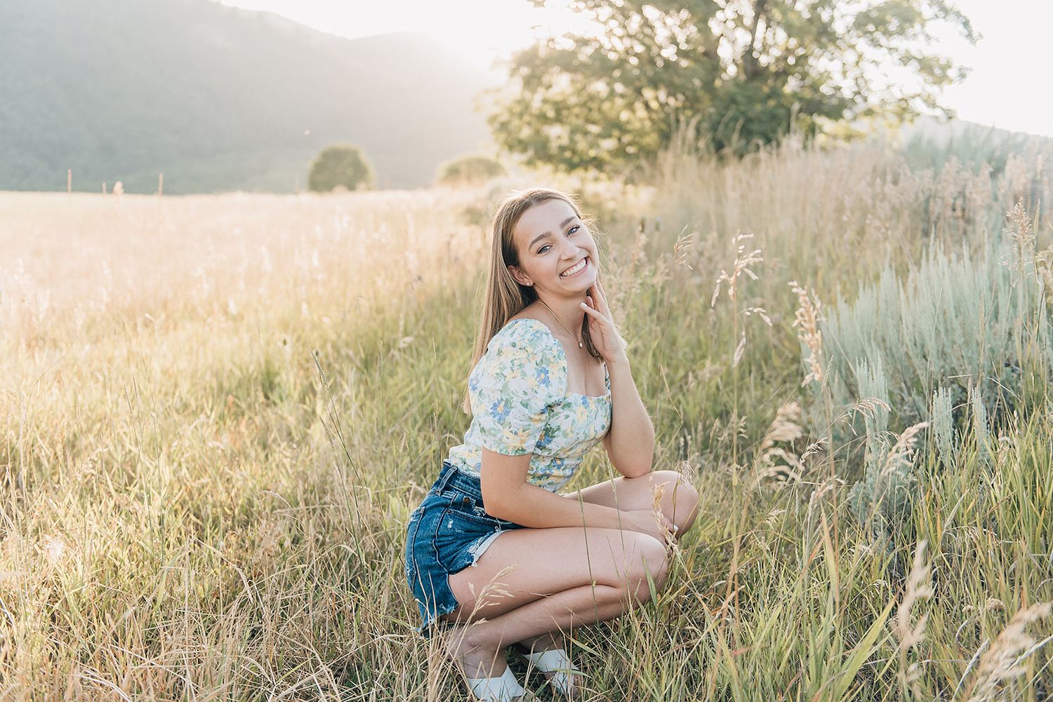 A person sits in a sunny field during golden hour wearing denim shorts and a blue top.
