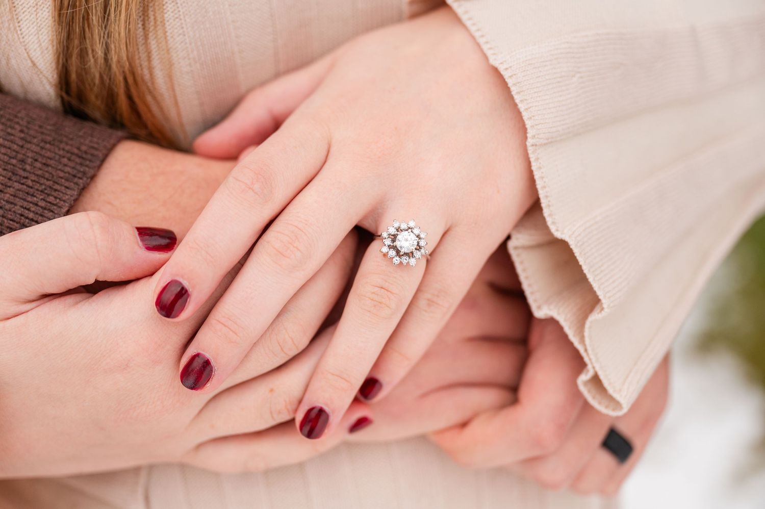 Close-up of engagement ring with red manicured nails on hands.