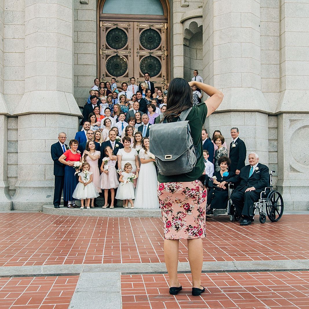 A photographer captures a group wedding photo on church steps.