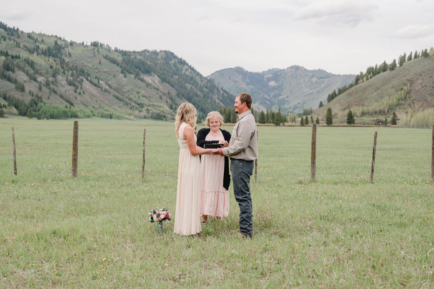 Outdoor elopement ceremony in a mountain meadow with couple and officiant, green hills backdrop.
