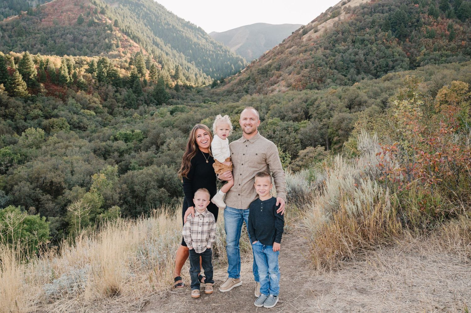 Family of five standing together on mountain trail during autumn season.