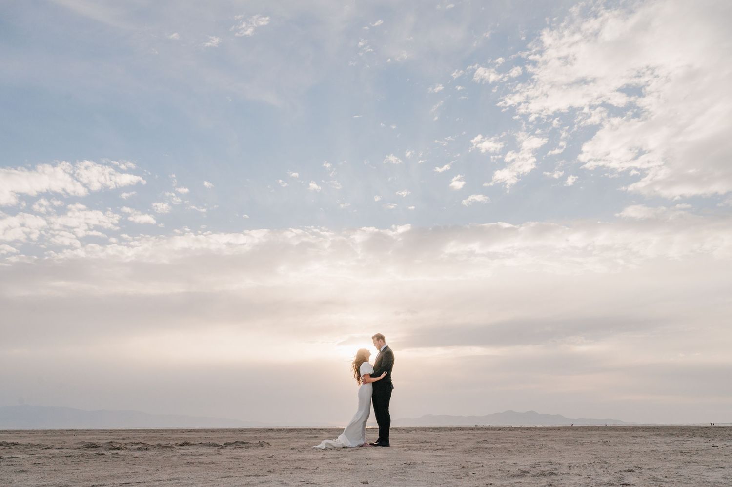 Romantic couple standing together on sandy beach during golden hour.