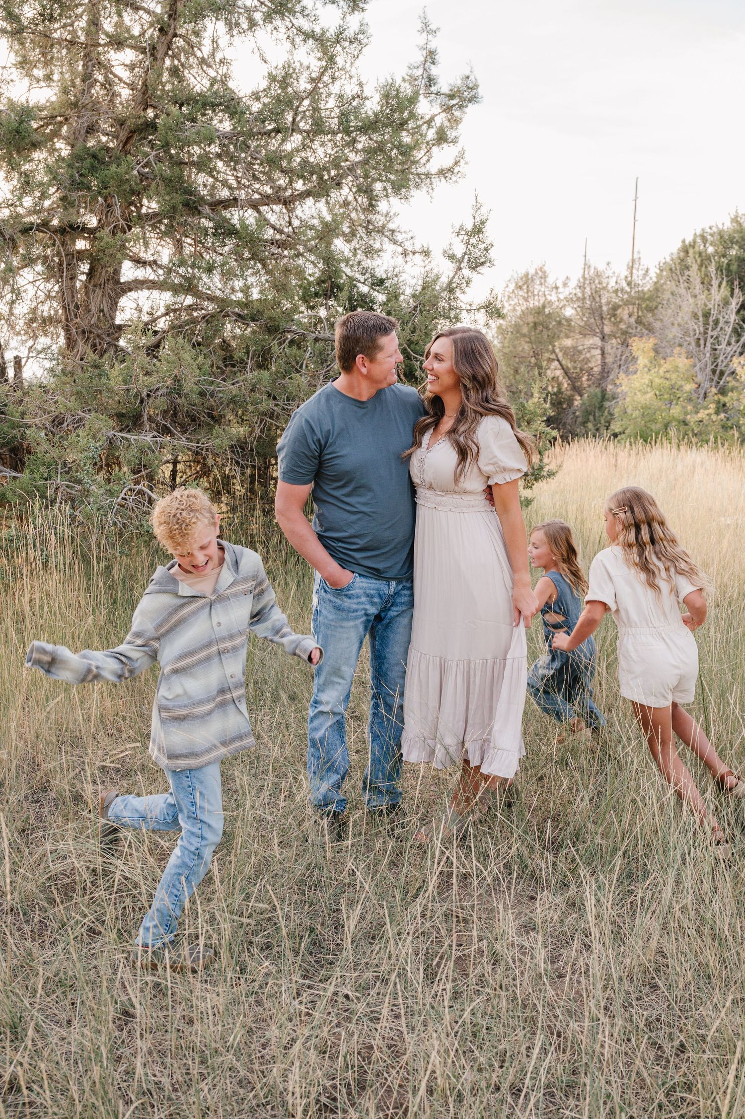 Family playing together in a golden field during sunset with children running and laughing.