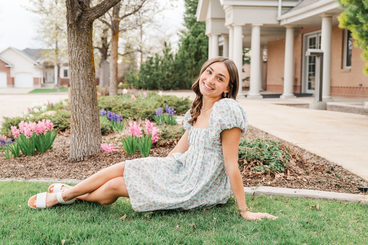 Person in floral dress relaxing on grass near blooming spring tulips and colonial style building.