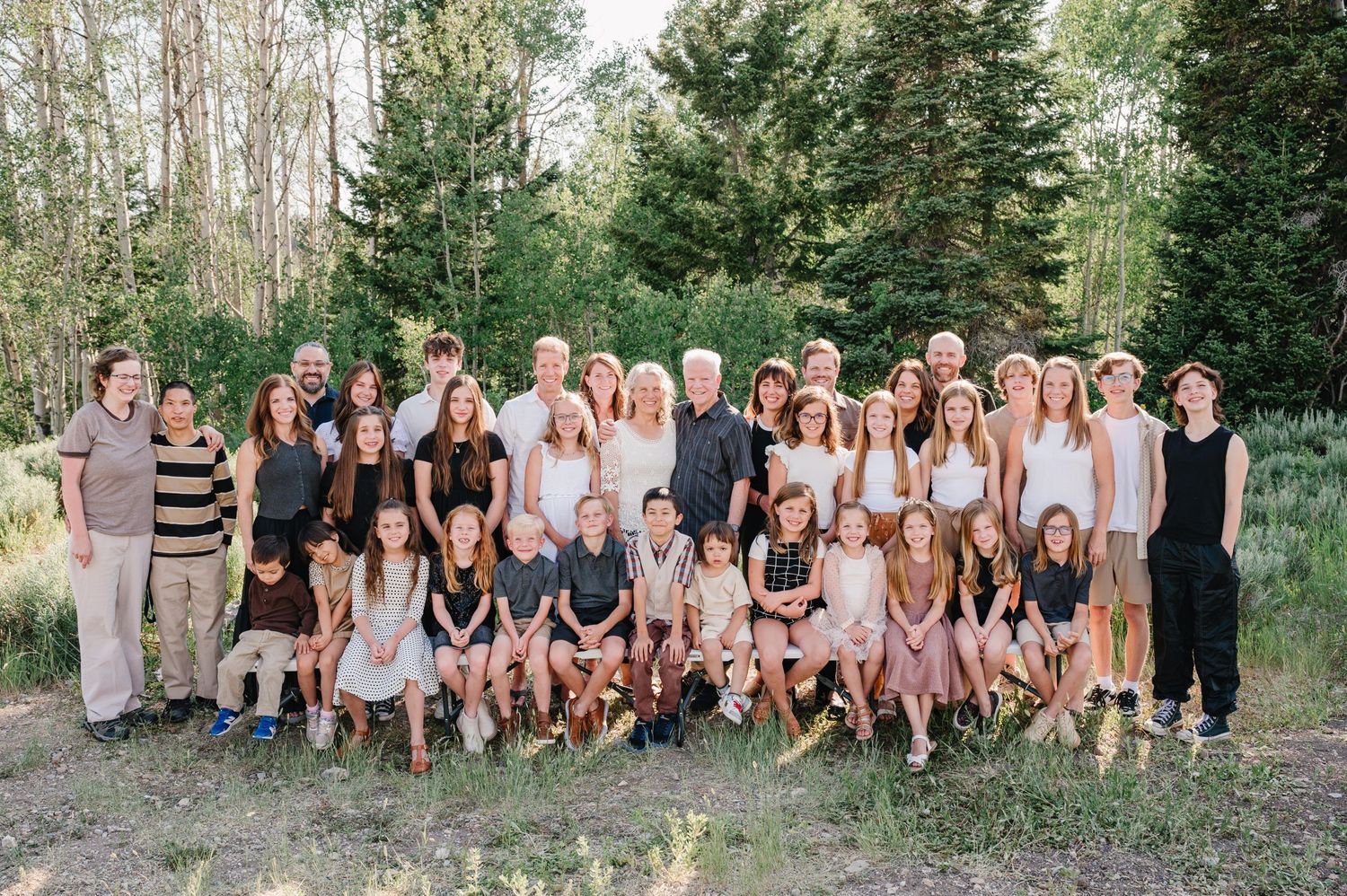 Large group photo with everyone wearing black and neutral colors in a mountain forest setting.