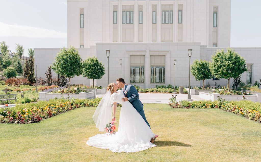 A wedding couple poses for romantic photos on a lush green lawn with a white building in the background.
