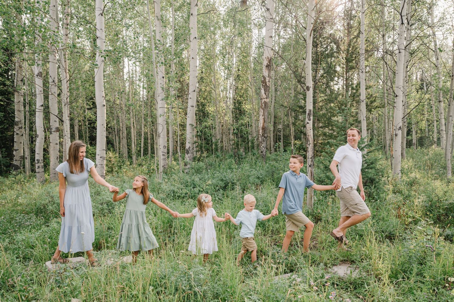 A line of people holding hands walking through a dreamy aspen forest.