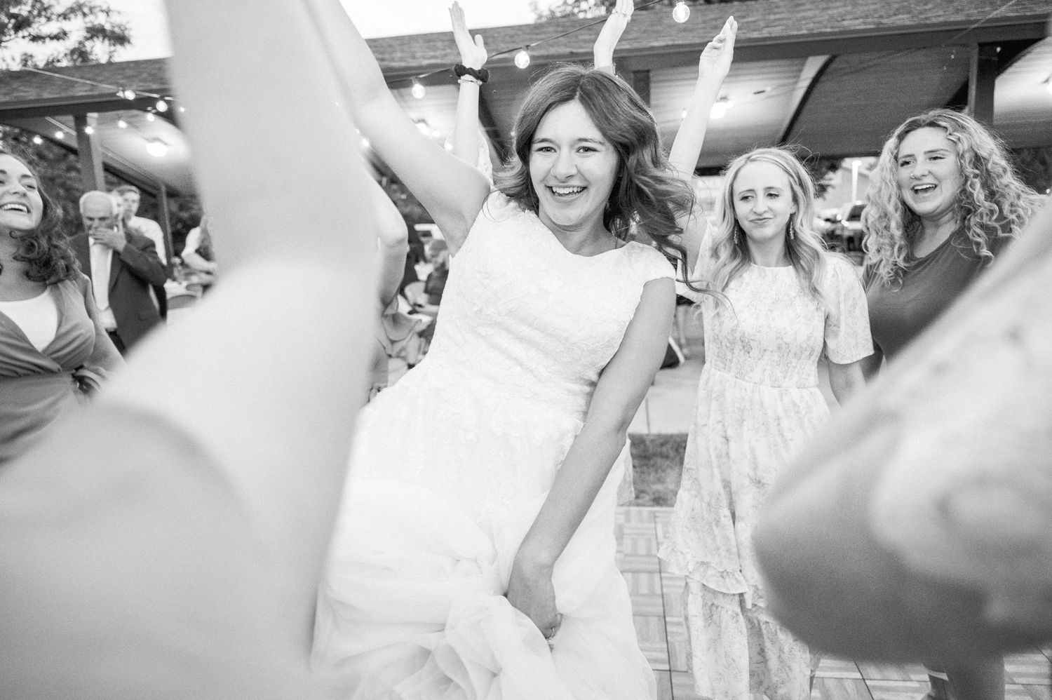 Black and white photo of joyful wedding celebration with dancing and raised hands.