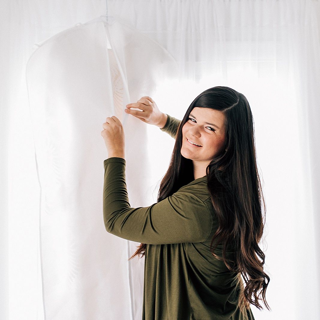 Photographer with long dark hair adjusts white backdrop in studio setting.