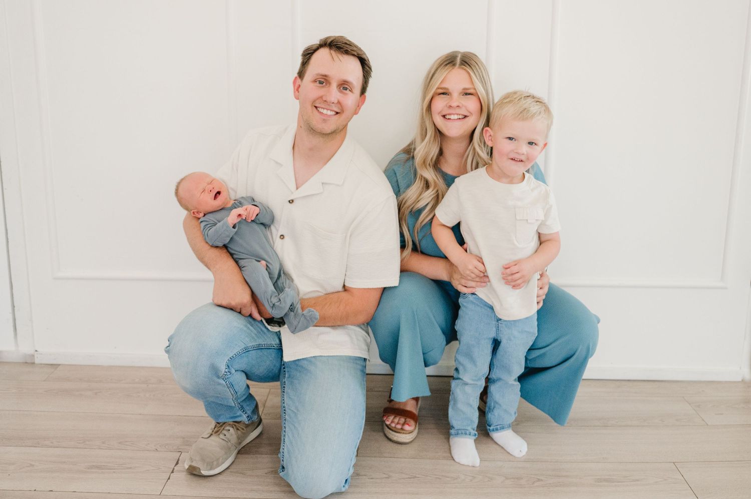 Young family sitting together on white floor wearing coordinated casual outfits.