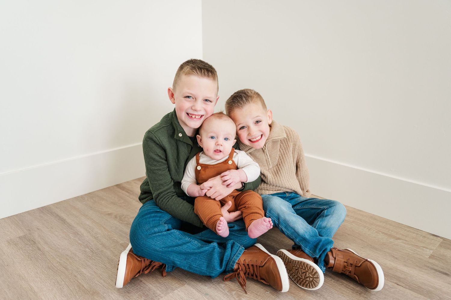 Three young children sitting together on wooden floor sharing a sweet moment.