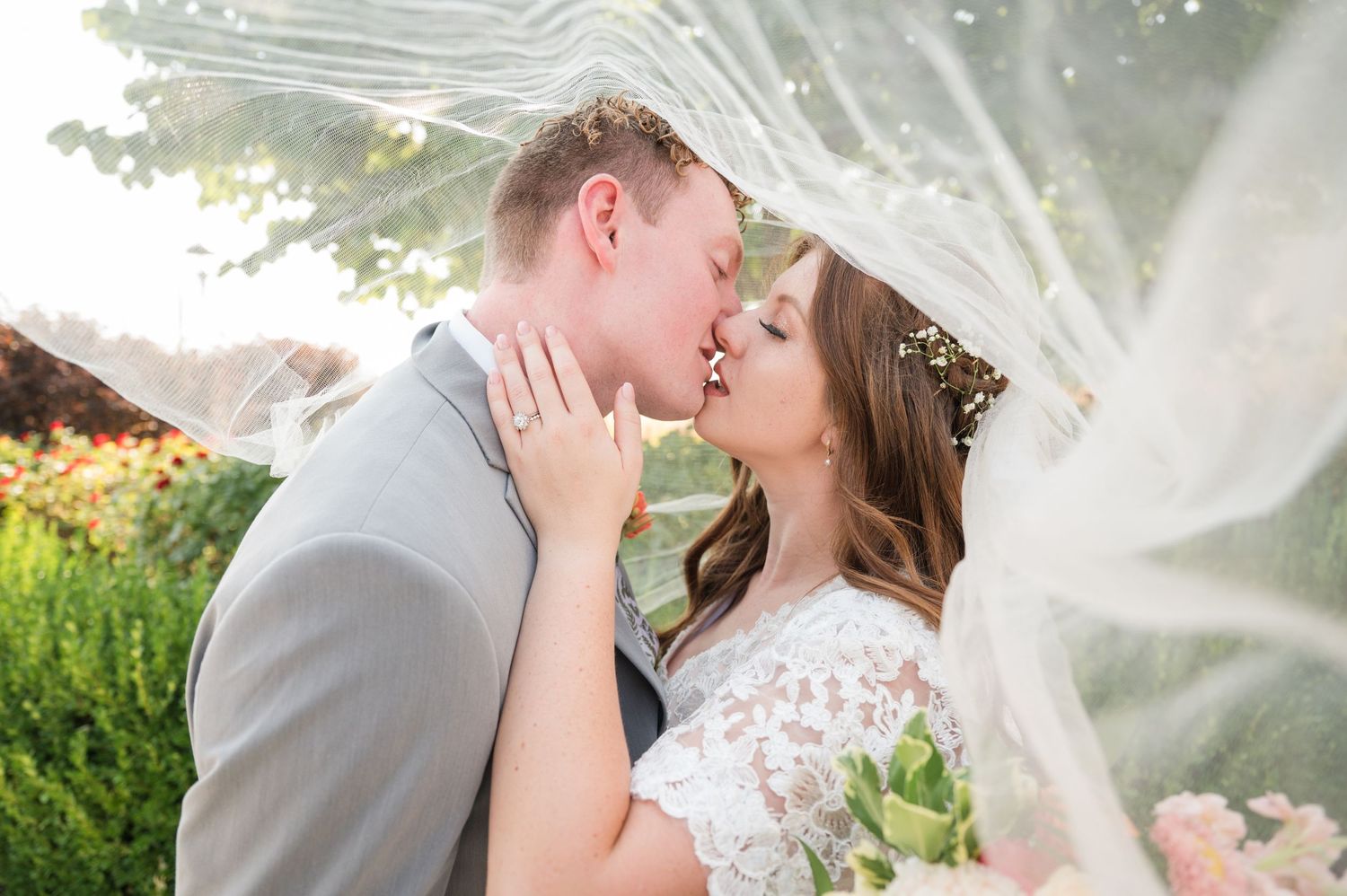 A romantic wedding scene with flowing veil and floral lace dress captured in soft natural lighting.