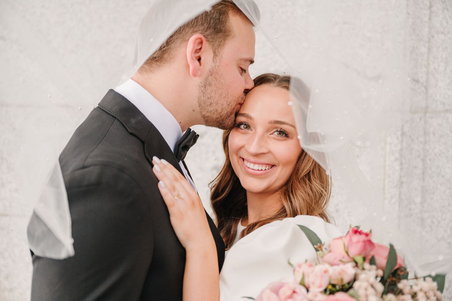 Intimate close-up of newlyweds sharing tender moment with pink roses in foreground.