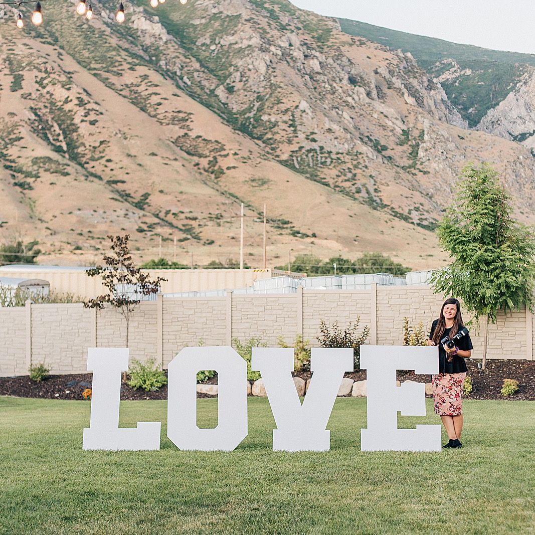 Large white LOVE letters displayed on grass with mountain backdrop.