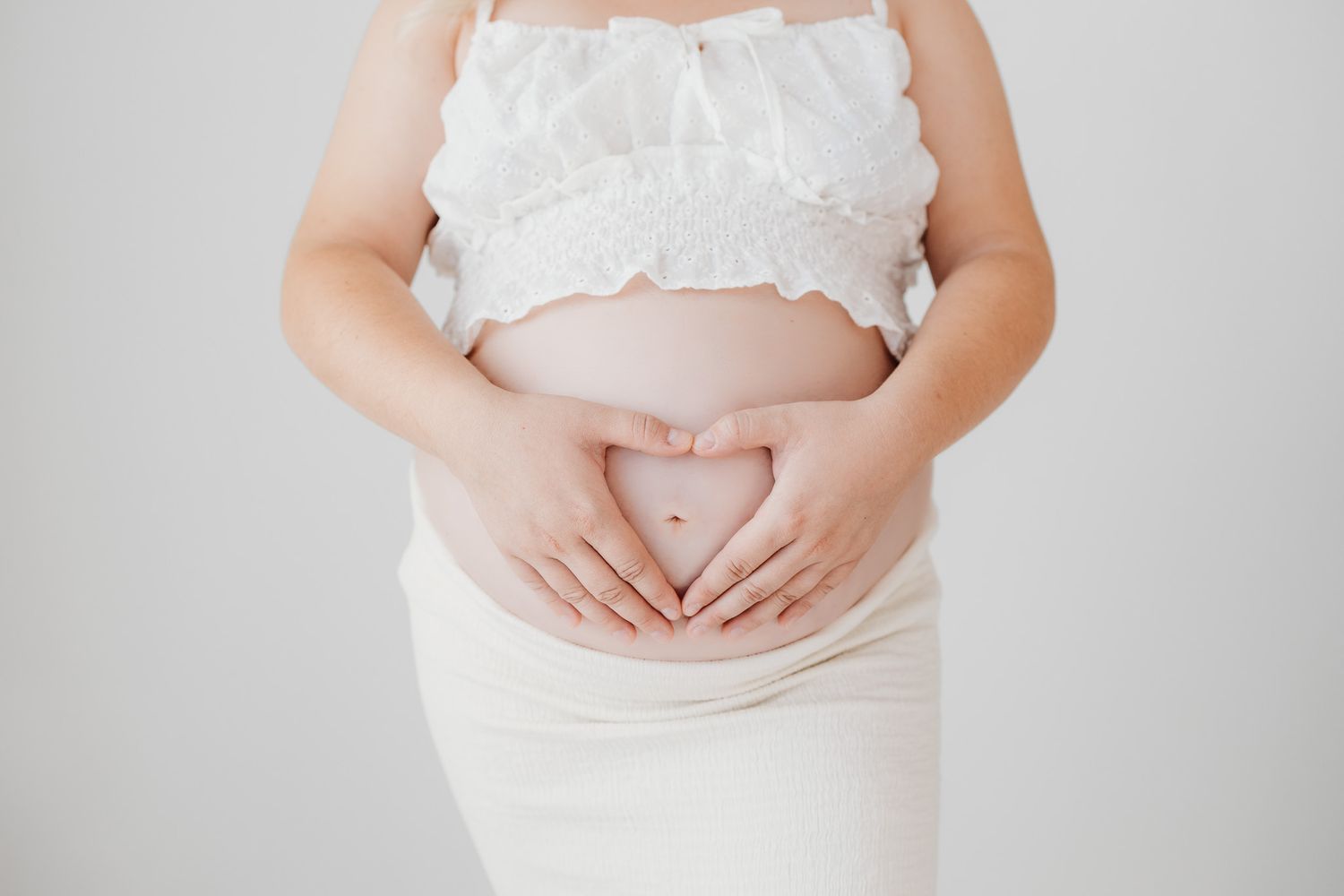 Photo of pregnant belly with hands in a heart over pregnancy belly. Photo from maternity photoshoot in Santa Fe, New Mex