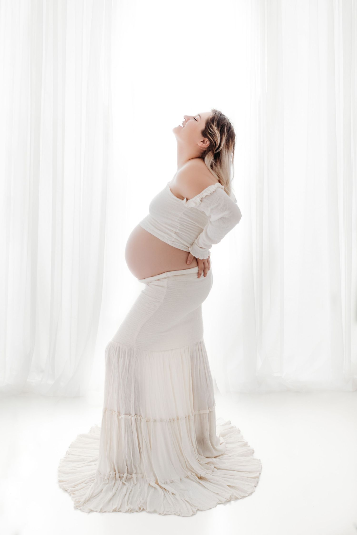 Boho and natural pregnant mother posing for maternity photos in front of light and curtains. Maternity photos in Santa F