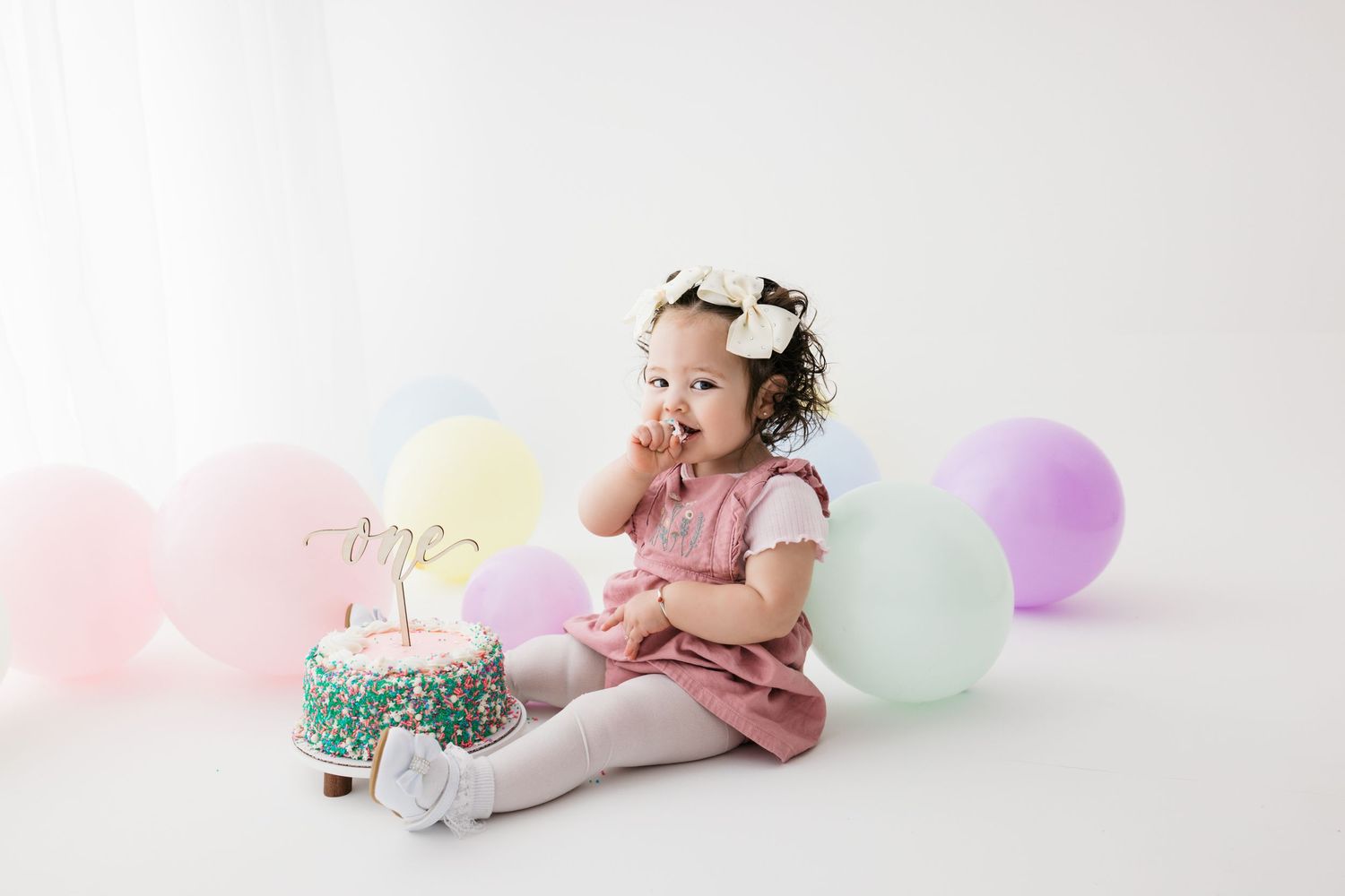 Little girl eating a pink cake for her first birthday photography session in Santa Fe. From Albuquerque and Los Alamos