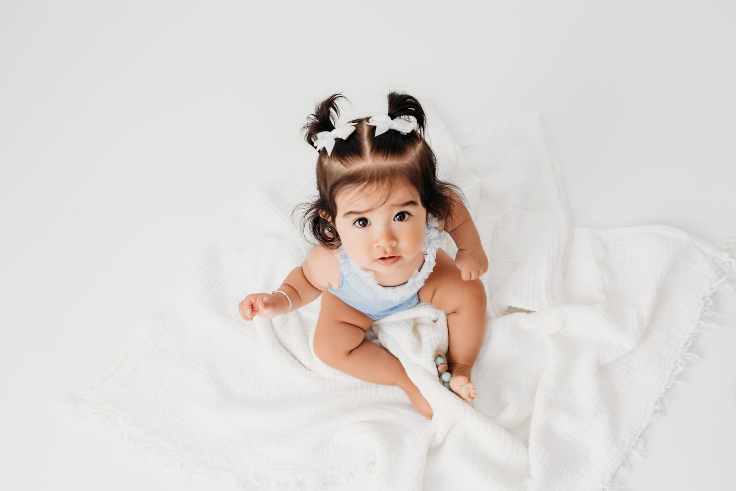 Photo of 8 month old baby sitting for photographer in Santa Fe, New Mexico. Cute little girl with pigtails and bows