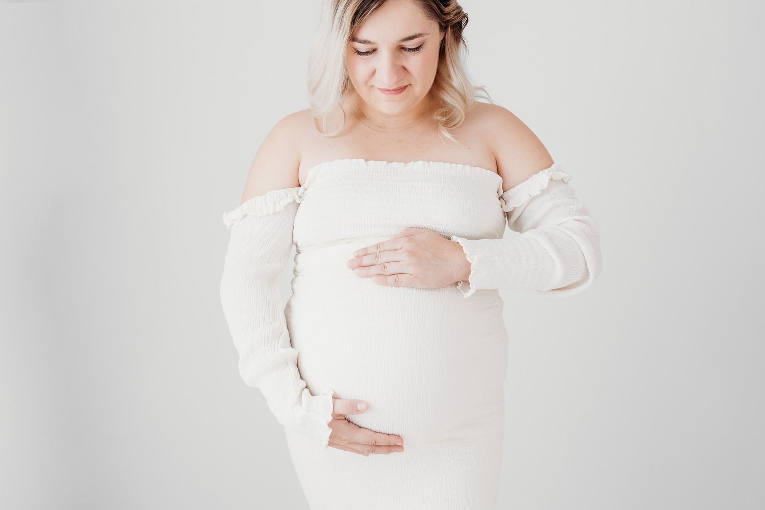 Pregnant woman looking down holding her baby belly in a boho minimalist photography studio. In a maternity session in ph