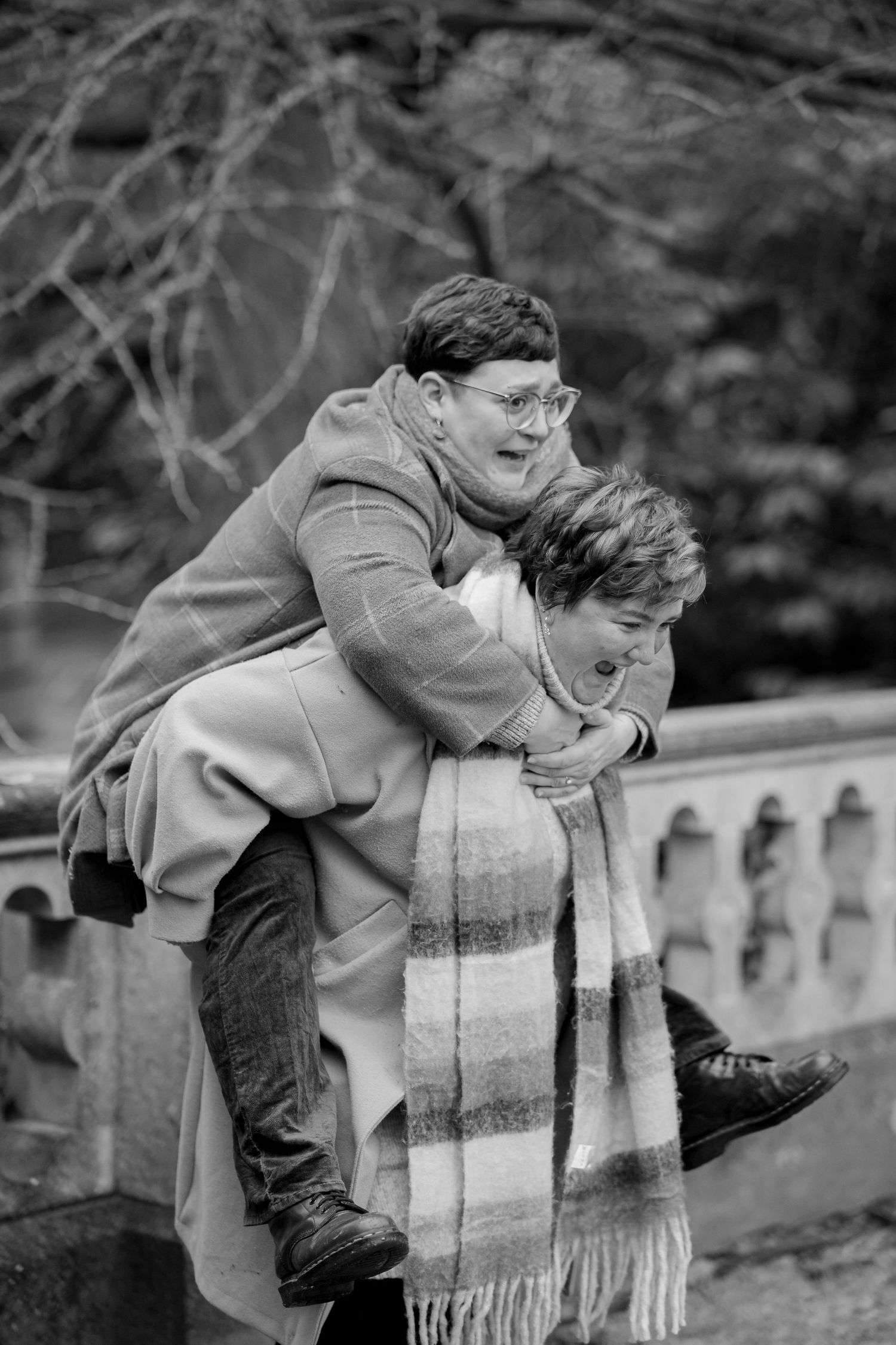 Two people share a playful piggyback ride moment outdoors in winter, wearing cozy coats and a striped scarf.