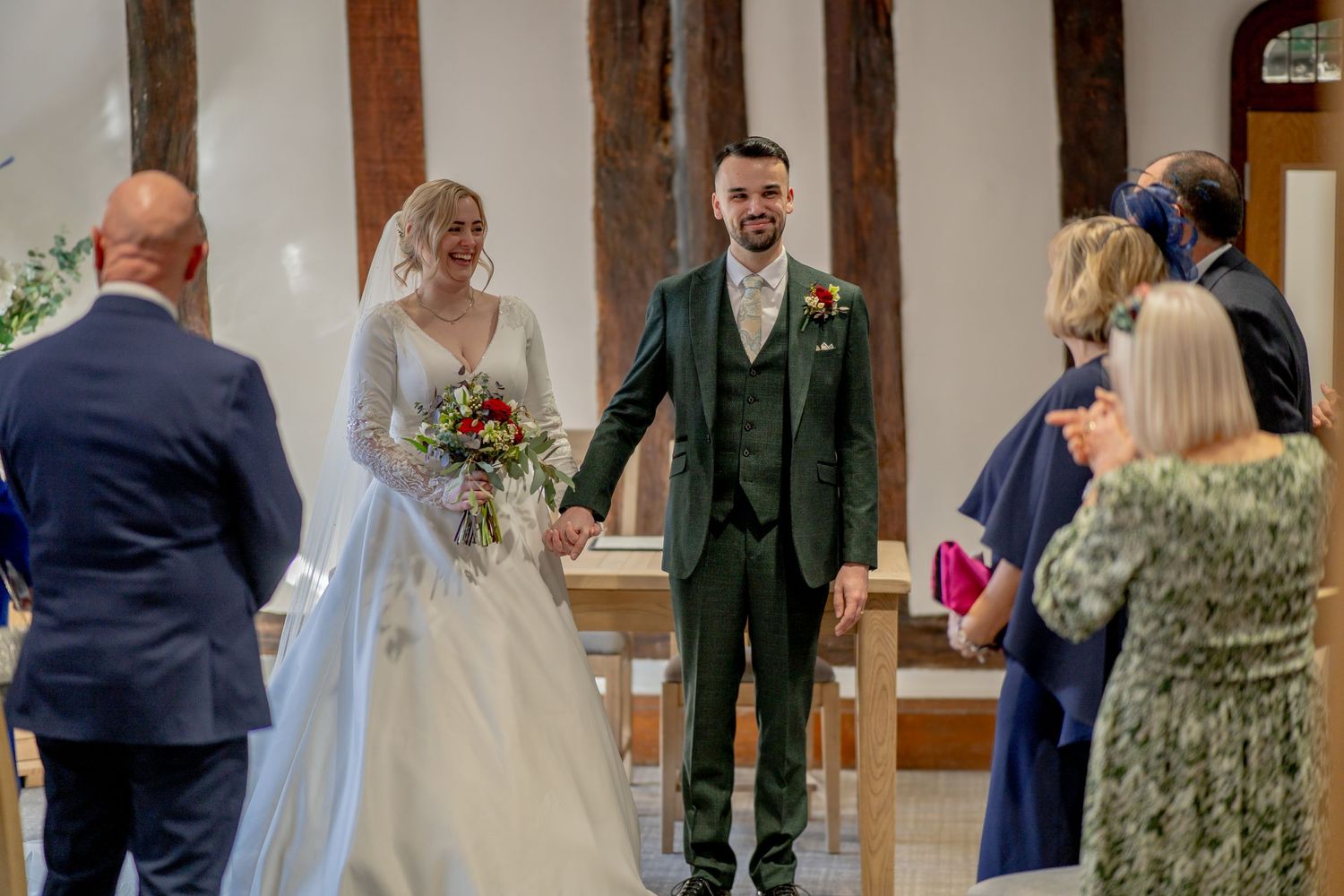 A wedding ceremony takes place in a church with exposed wooden beams and white walls.