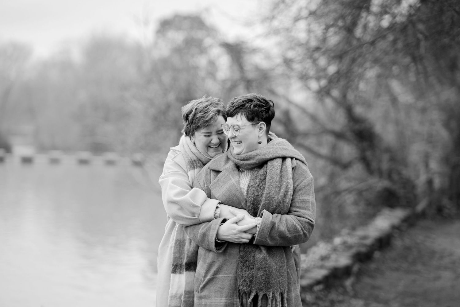 A black and white photograph of a couple embracing beside a lake on a misty day.