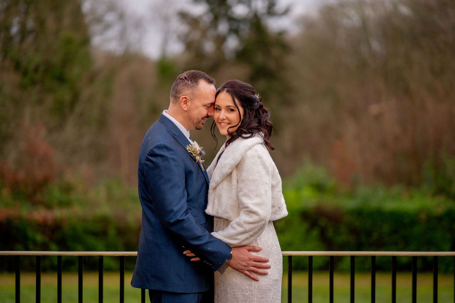 A happy couple embraces outdoors on a winter day, with the bride wearing a white wrap and groom in a navy suit.