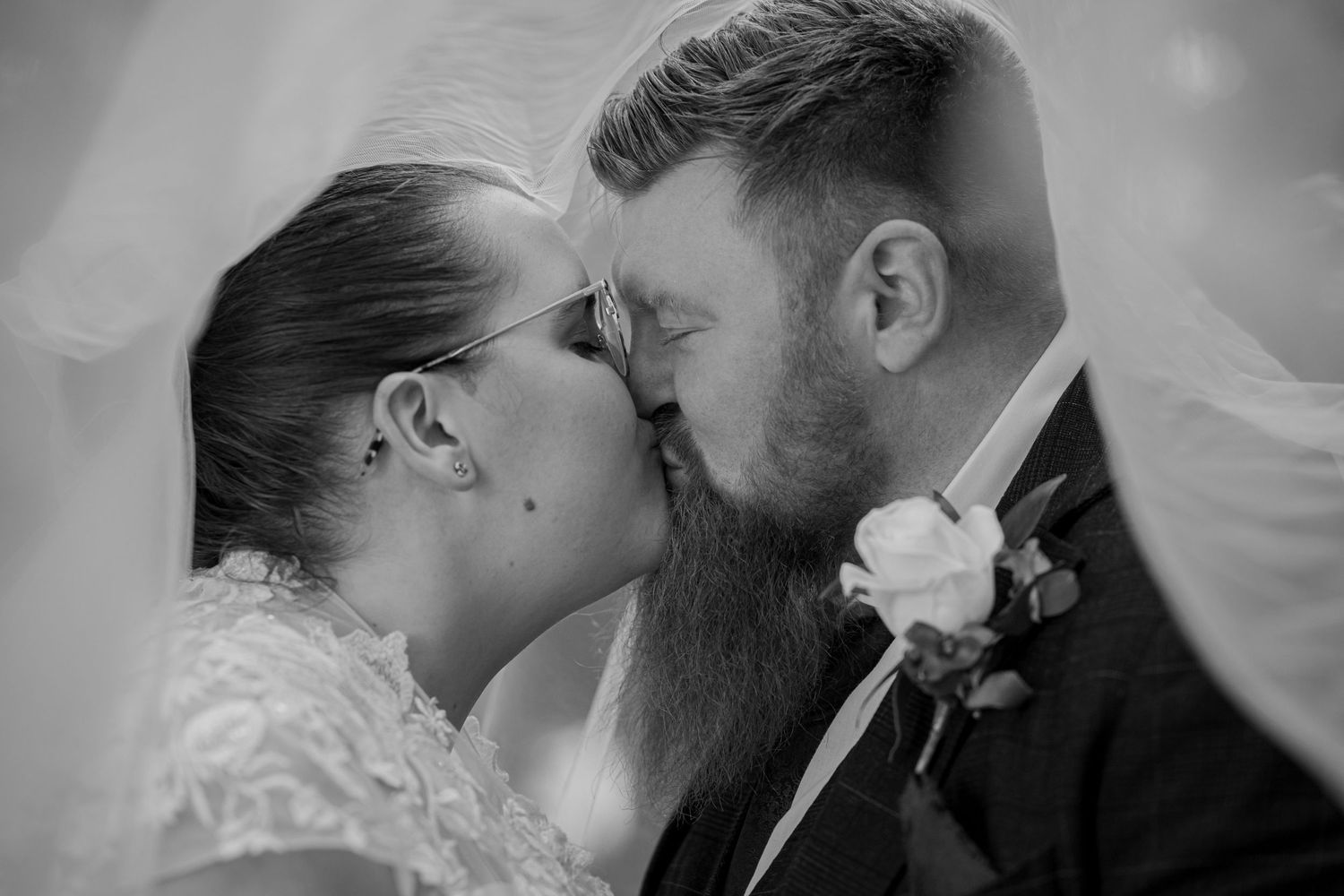 A romantic black and white photograph of a wedding couple sharing a tender kiss under a veil.