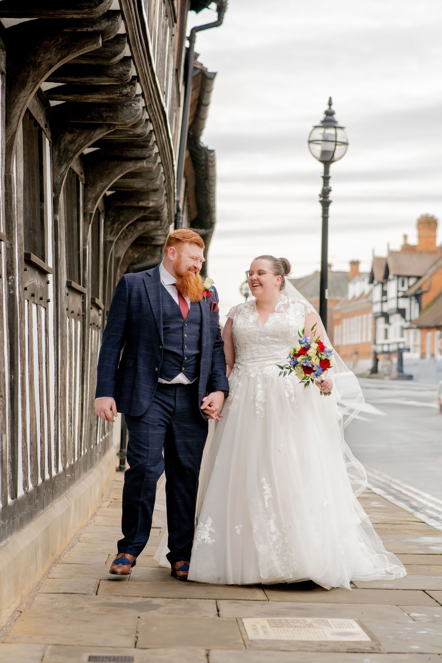 A couple shares a joyful moment on their wedding day while walking along a historic street with traditional architecture.